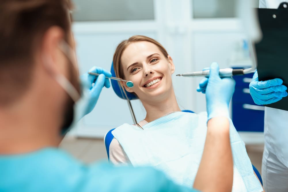 A young woman sits in a dental chair and smiles.